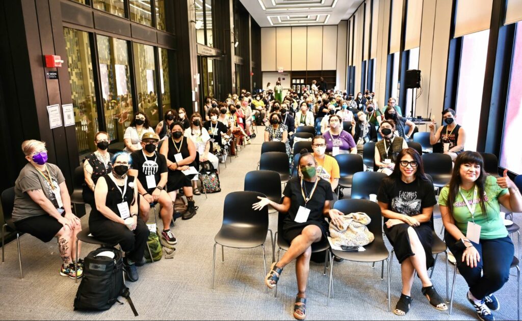 group photo of about 100 people sitting in chairs in a large university conference room.